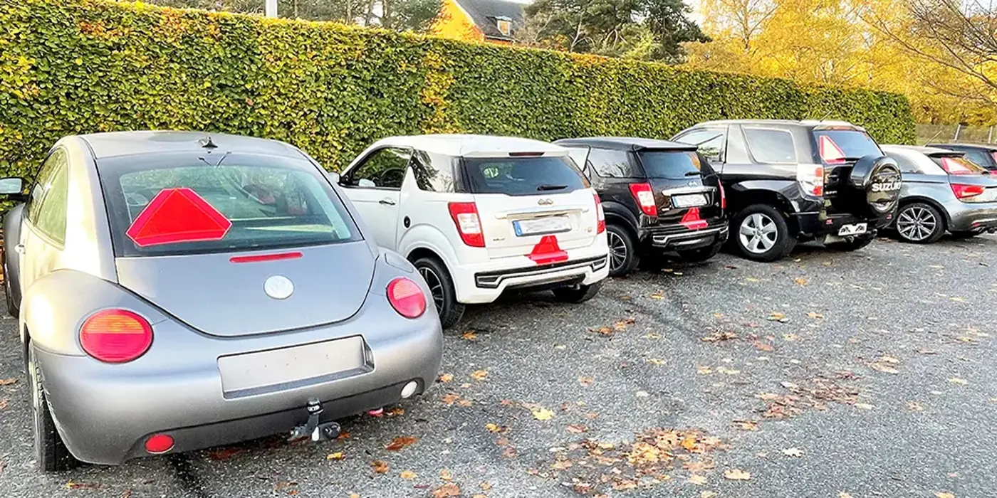 Fem A-traktorer och mopedbilar står parkerade på en parkeringsplats vid en hög häck.