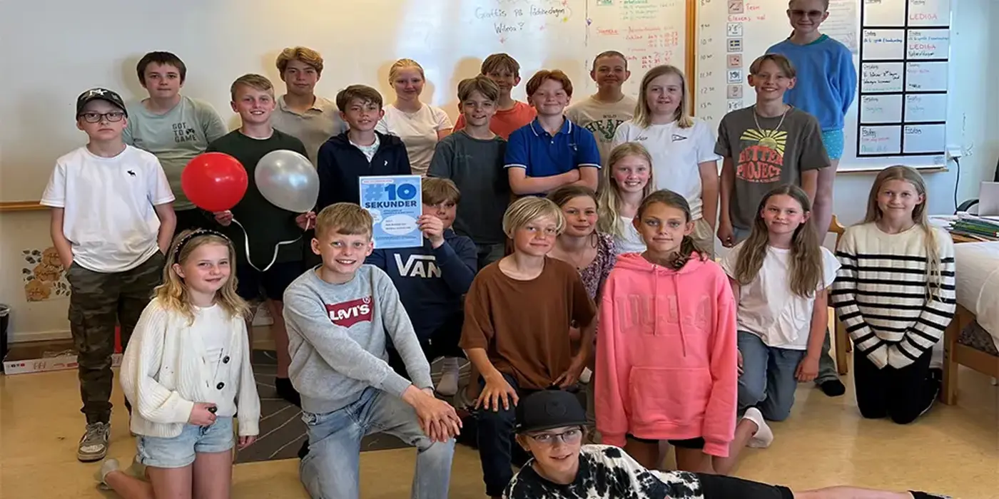 En skolklass står framför en whiteboardtavla och håller upp ett diplom.