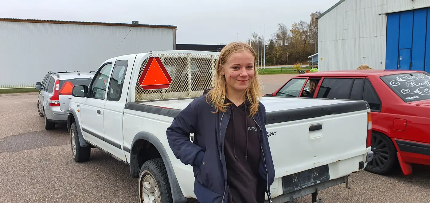 En ung kvinna står framför en A-traktor och ler mot kameran.