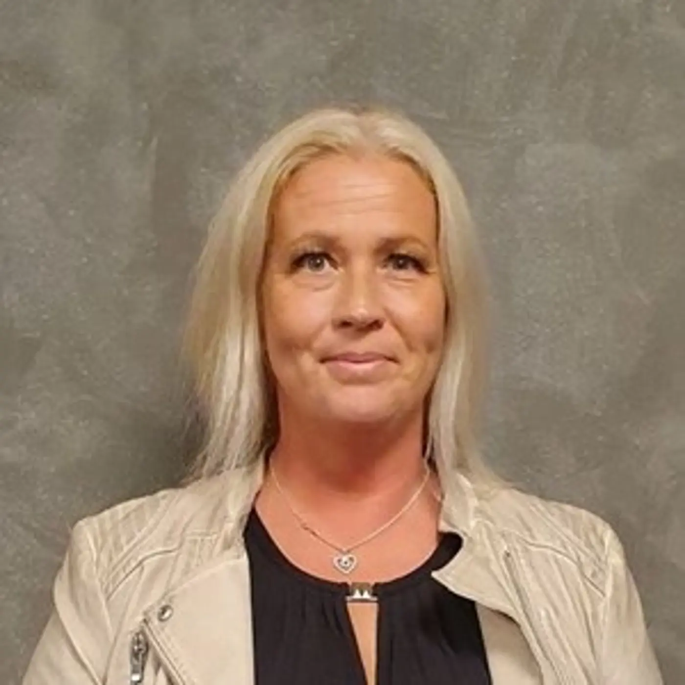 En leende kvinna med blont hår och ljus skinnjacka.