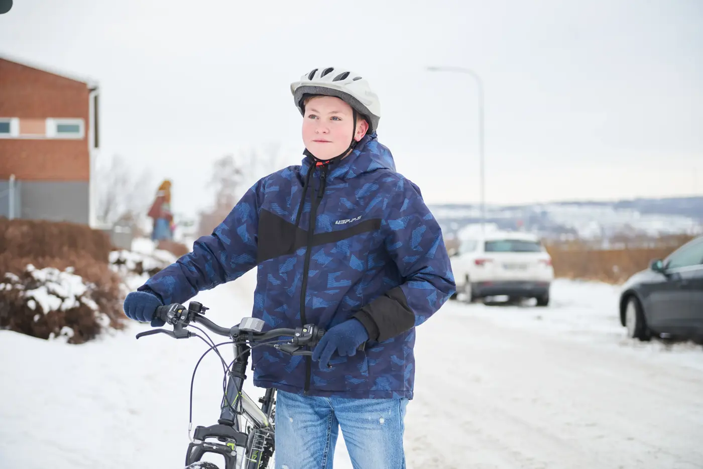 Tonåring står med en cykel i vintrig miljö.