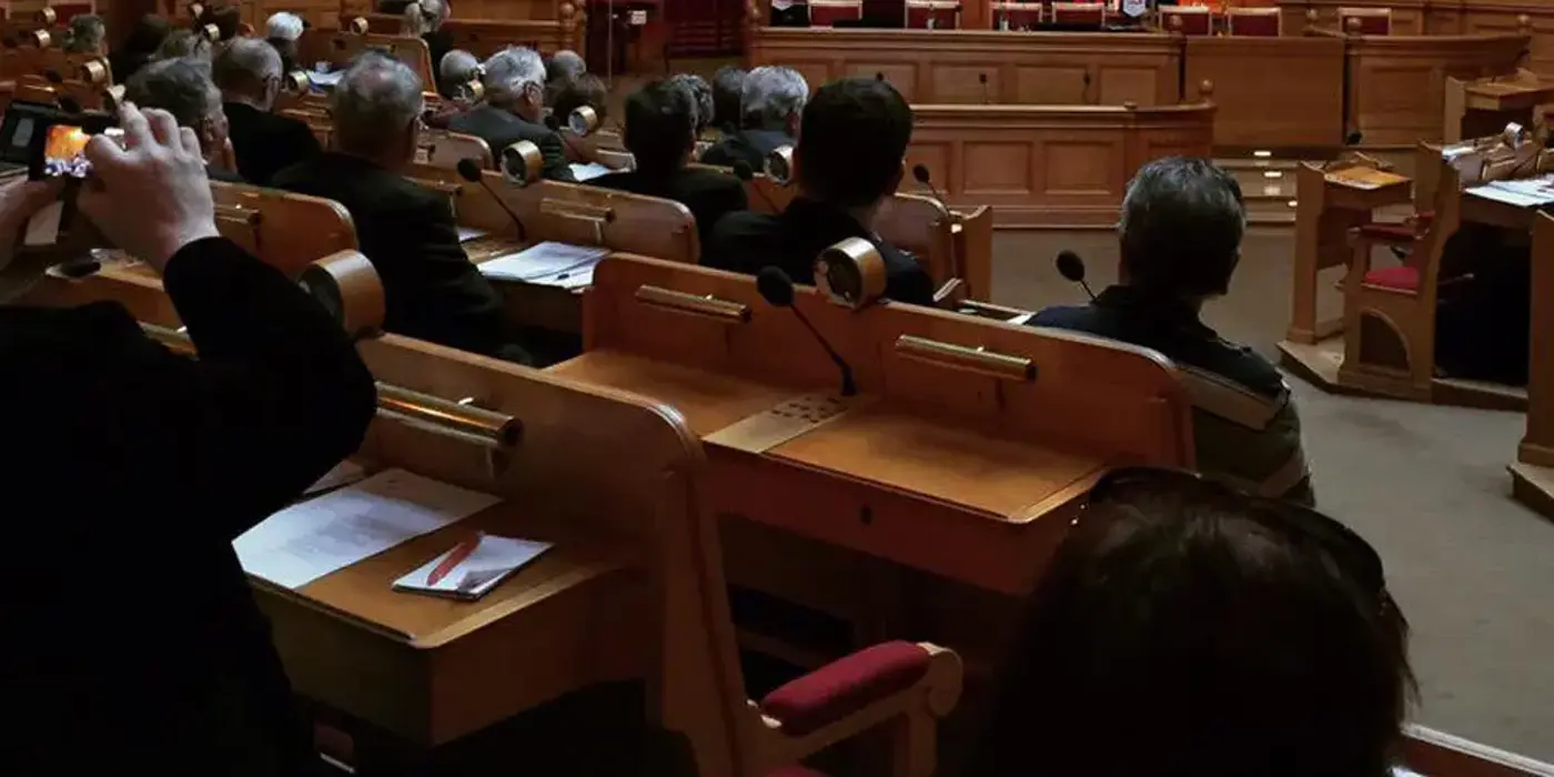 Förtroendevalda sitter vid bänkar med papper framför sig.