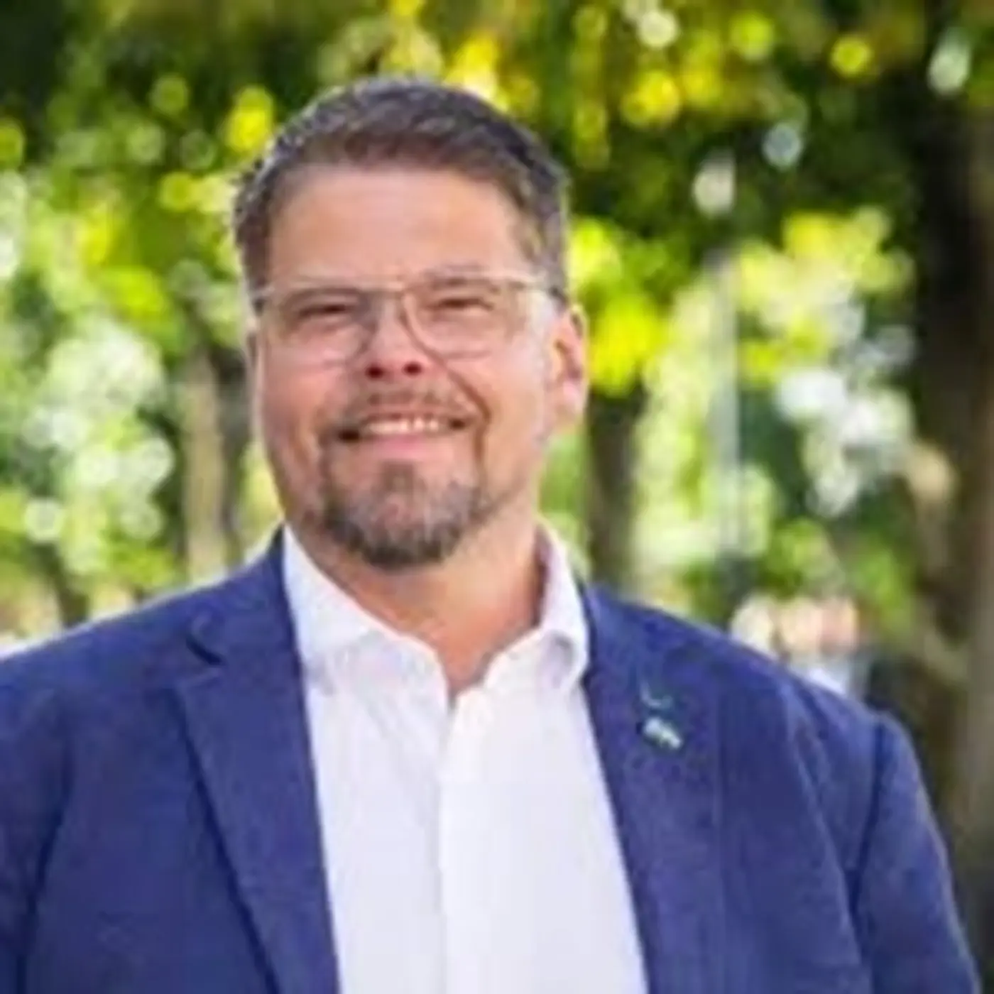 En leende man med glasögon, vit skjorta och blå kavaj.