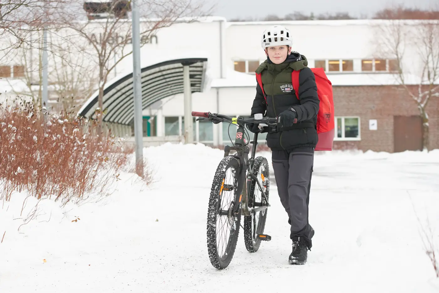 Ett barn leder sin cykel på en snöfylld skolgård