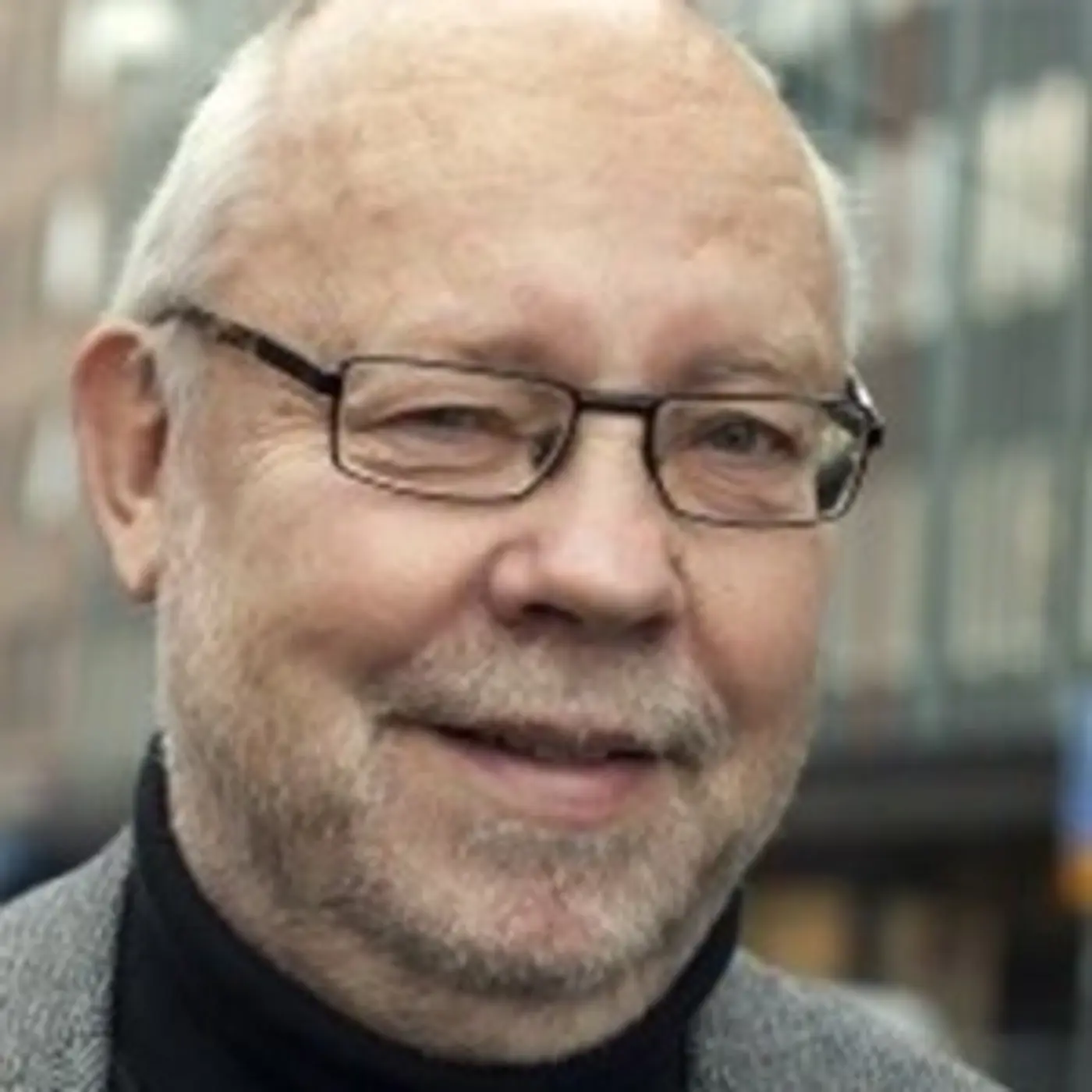 En leende äldre man med glasögon och svart polotröja.