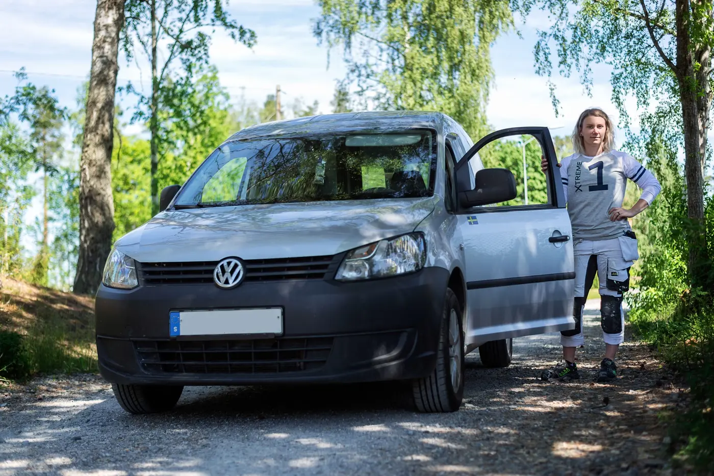 En kvinnlig hantverkare med målarbyxor står bredvid en skåpbil.