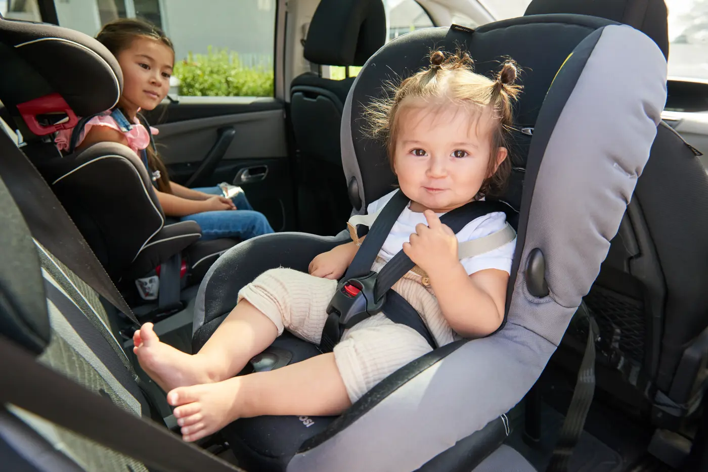 Två barn sitter i varsin bilbarnstol i baksätet på en bil, det lite äldre barnet sitter framåtvänt och det yngre är placerad i en bakåtvänd stol.