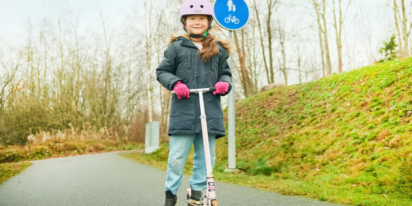 Ett barn med hjälm på huvudet kör sparkcykel på en gång-och cykelbana.
