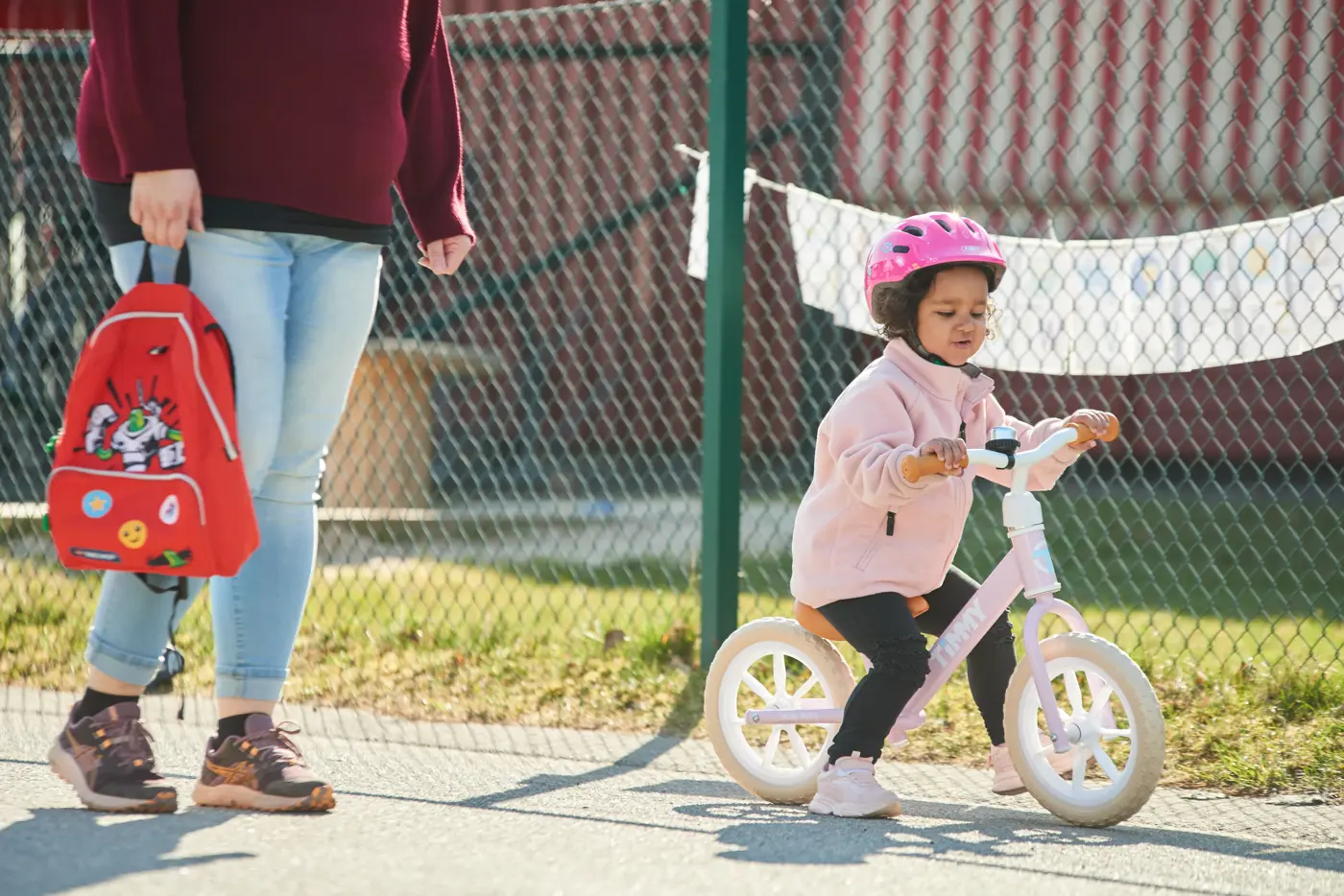 Ett småbarn med hjälm på huvudet kör balanscykel utanför en förskola.