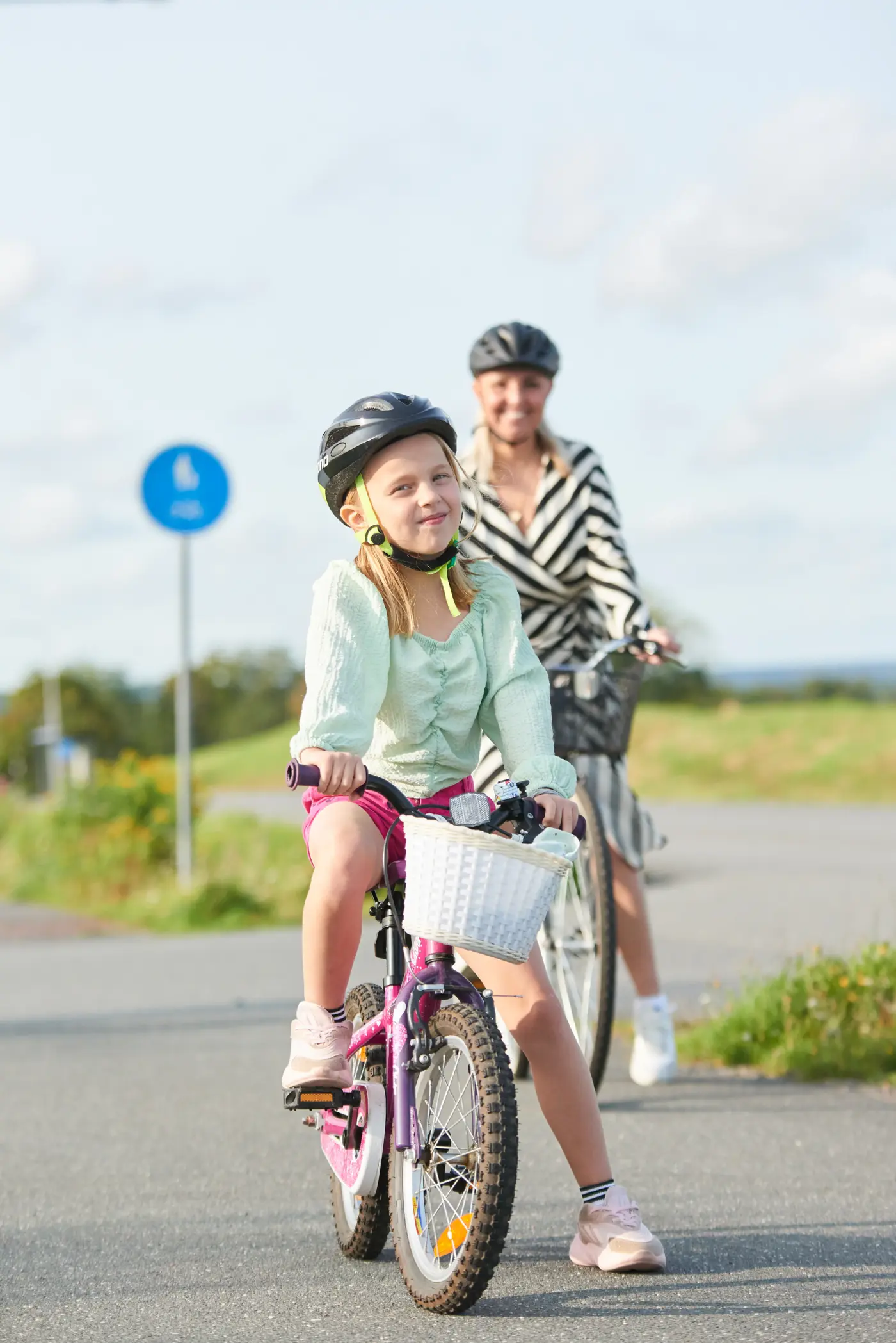 Vuxen och barn som är ute och cyklar på cykelbana, sommartid. Båda har hjälm på huvudet.