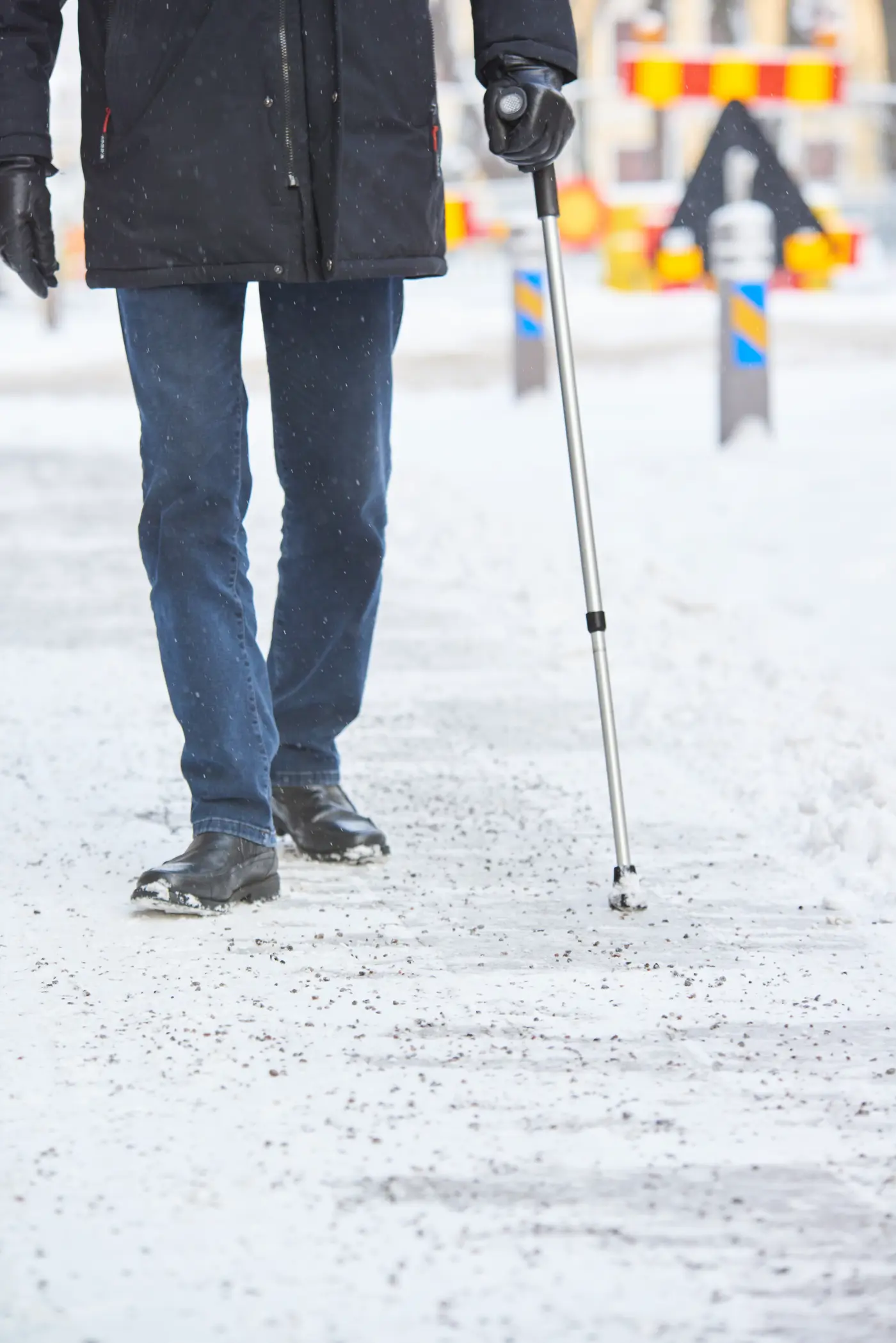 En äldre person promenerar med en käpp på en snötäckt trottoar.