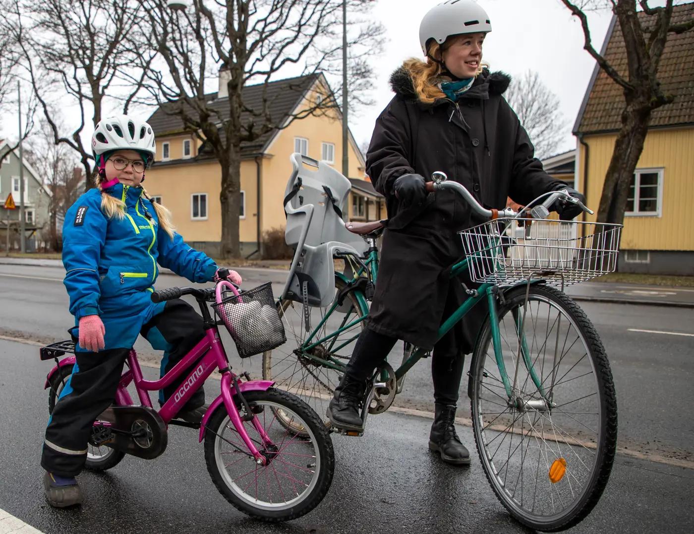 Ett barn och en vuxen på varsin cykel. Båda har hjälm på huvudet.