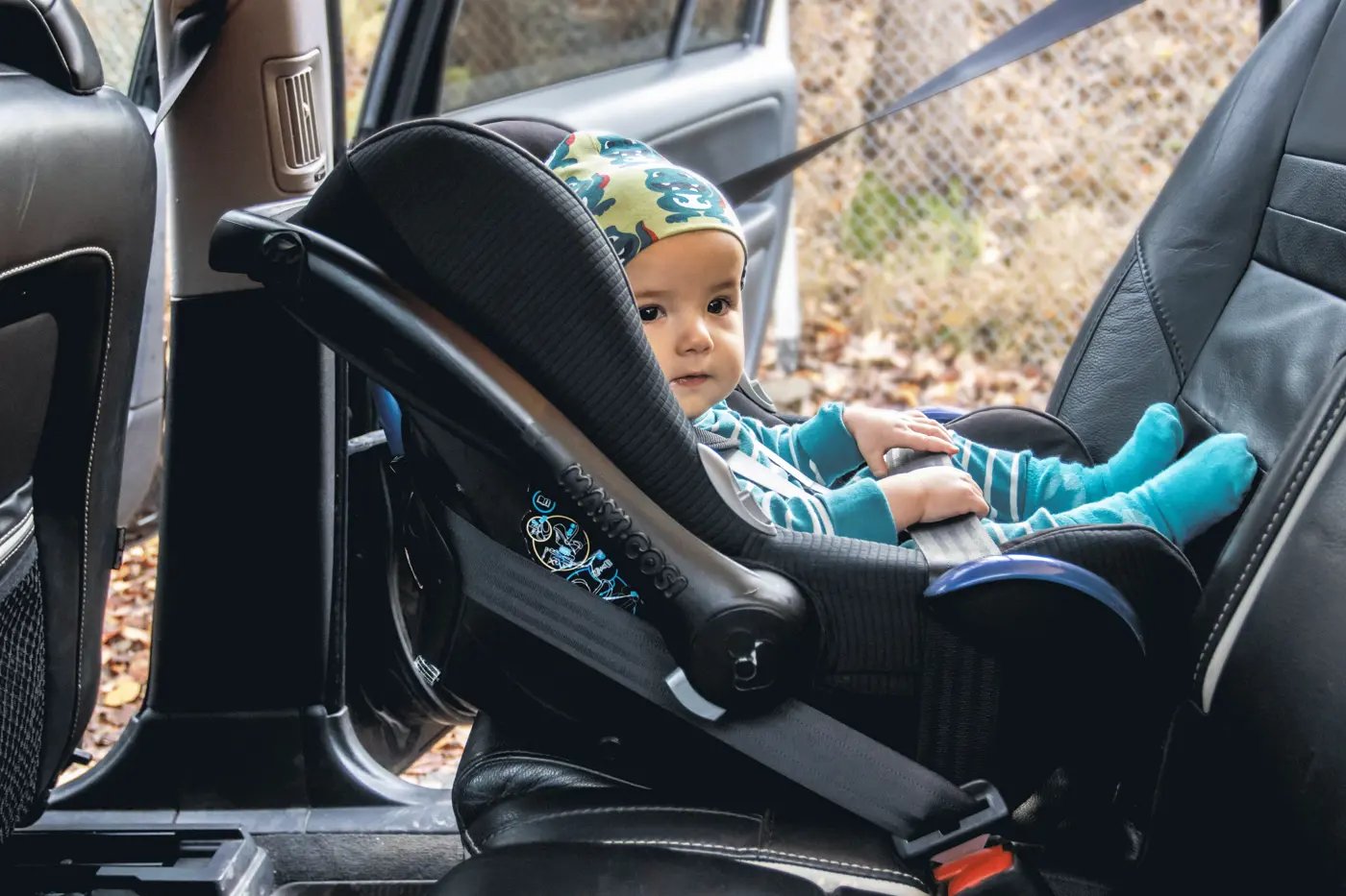 Ett småbarn sitter i ett babyskydd i baksätet på en bil.