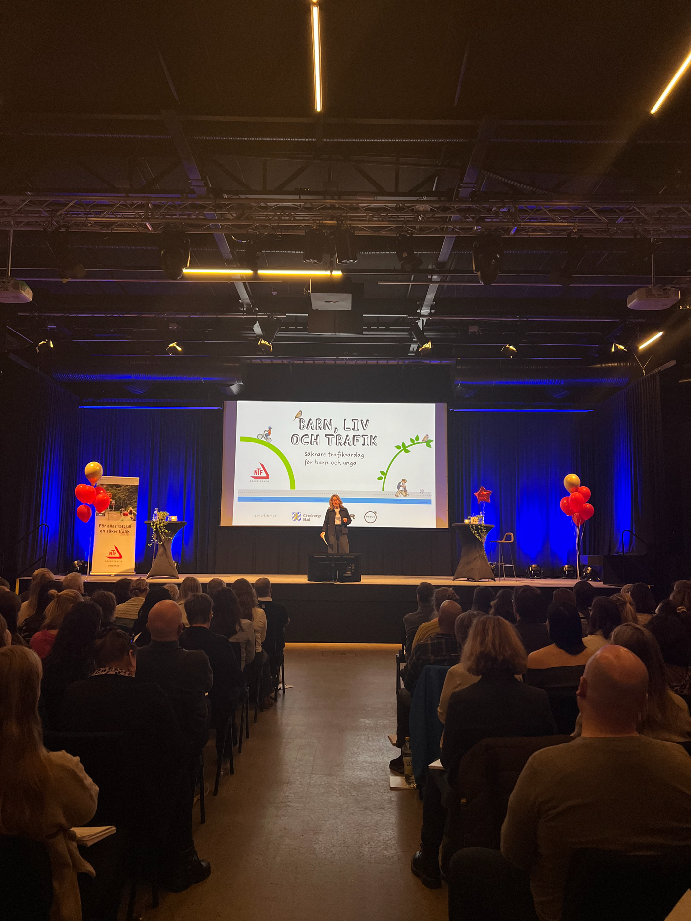 En kvinna står på en scen och framför sitter publik.