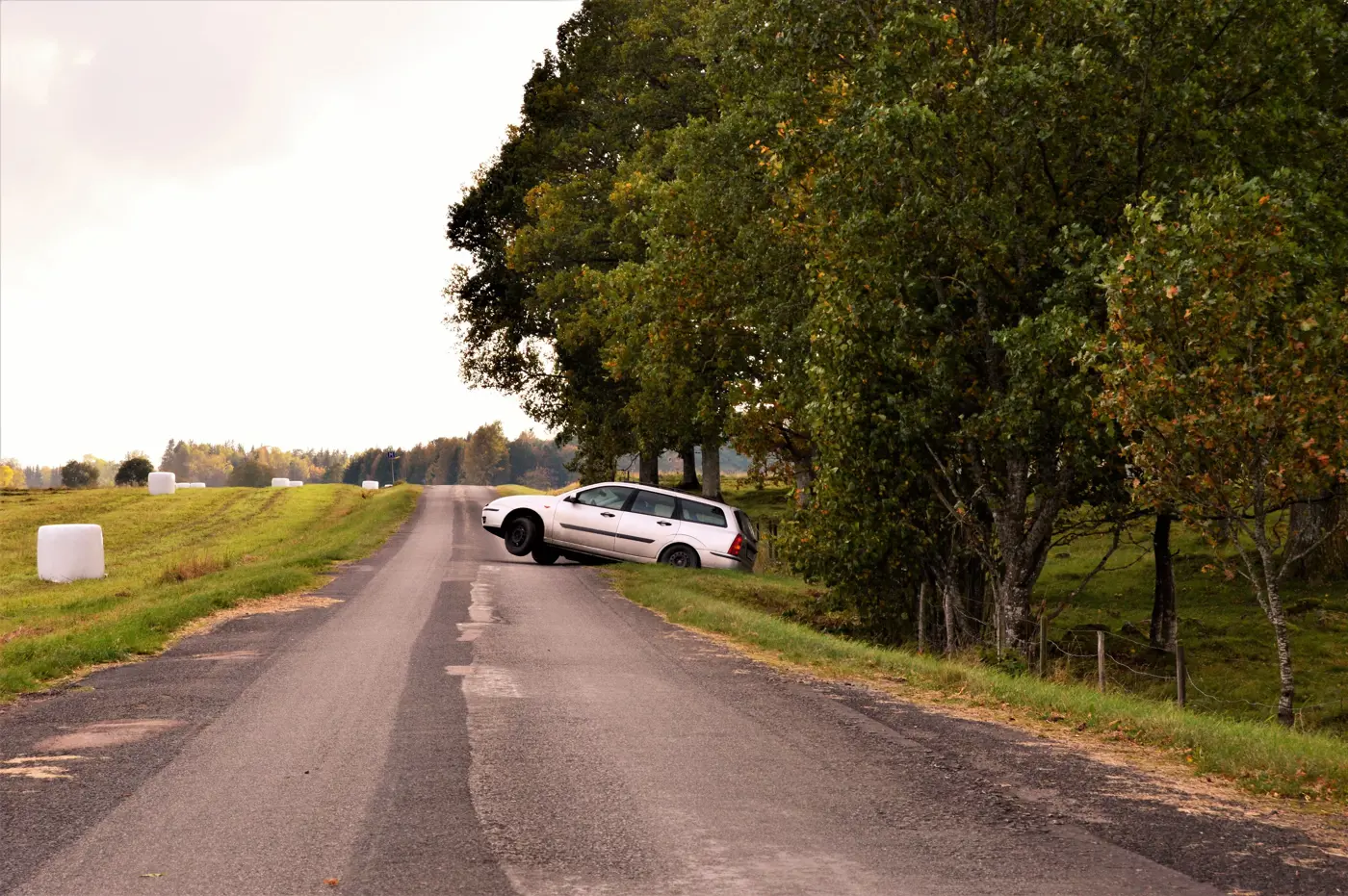 En bil ligger i diket på en asfalterad väg.