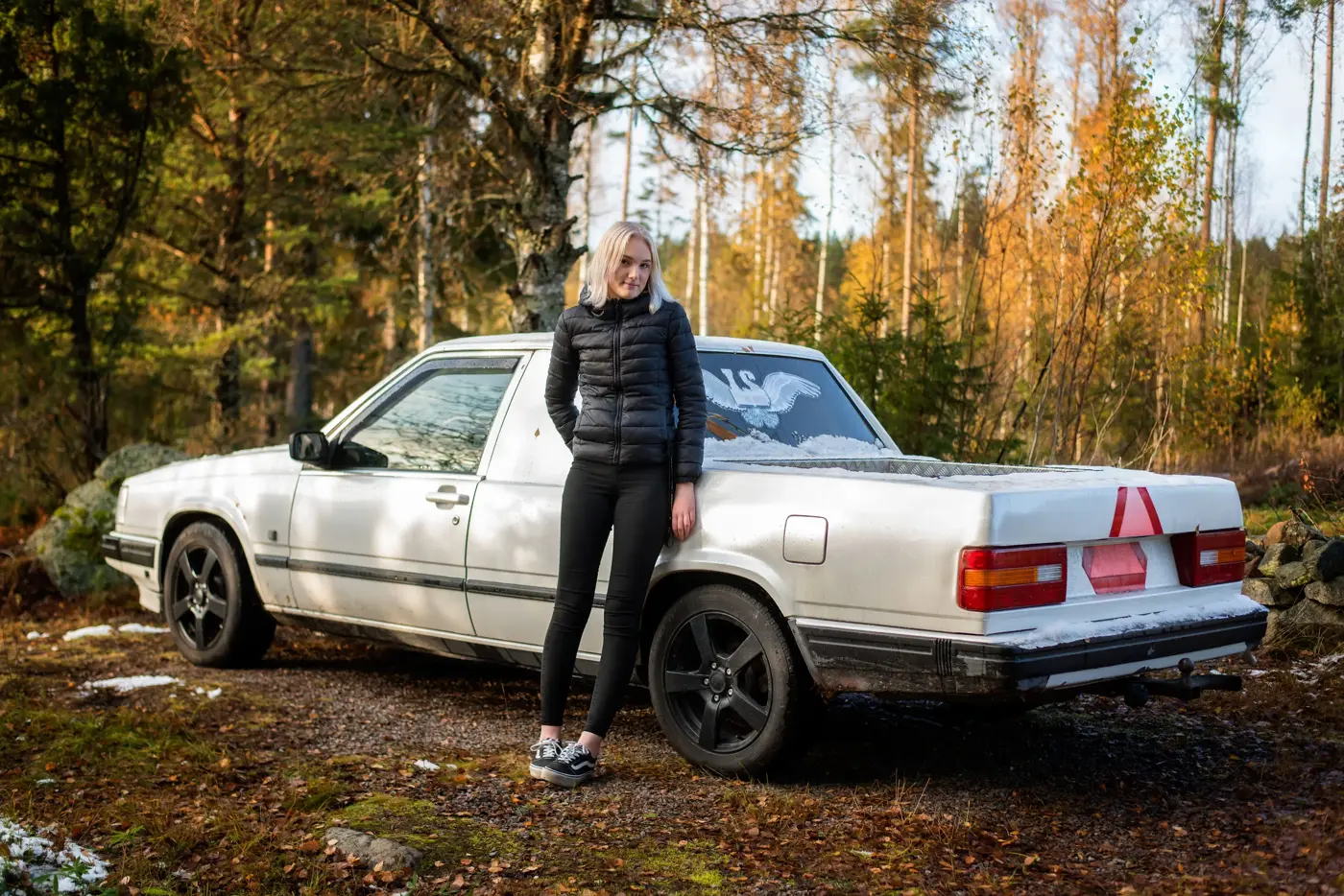 Ungdom lutar sig mot en vit A-traktor i skogen med blicken riktad mot kameran.