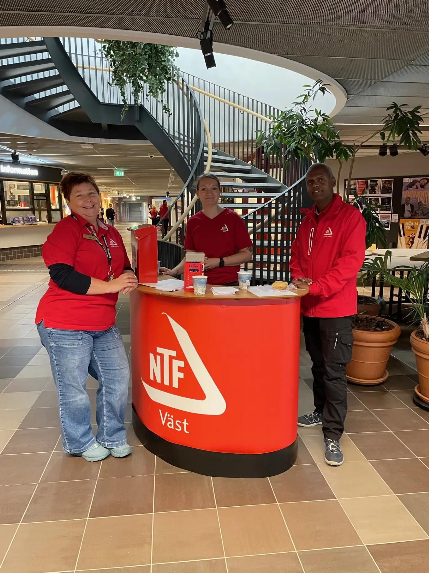 Tre personer med NTF-tröjor står vid ett bord och ler mot kameran.