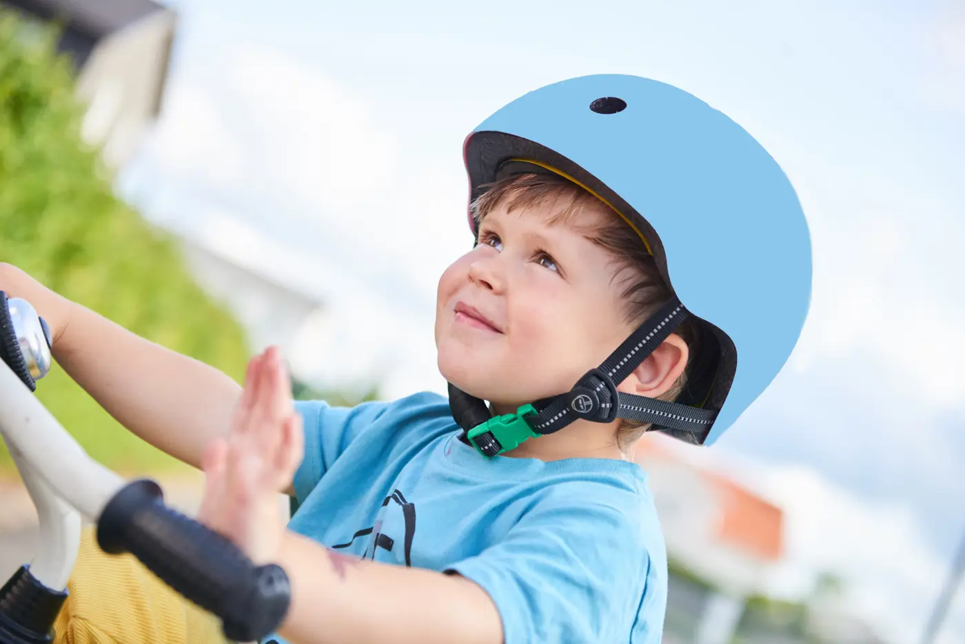 Ett barn sitter på en cykel med en cykelhjälm med grönt spänne på huvudet.