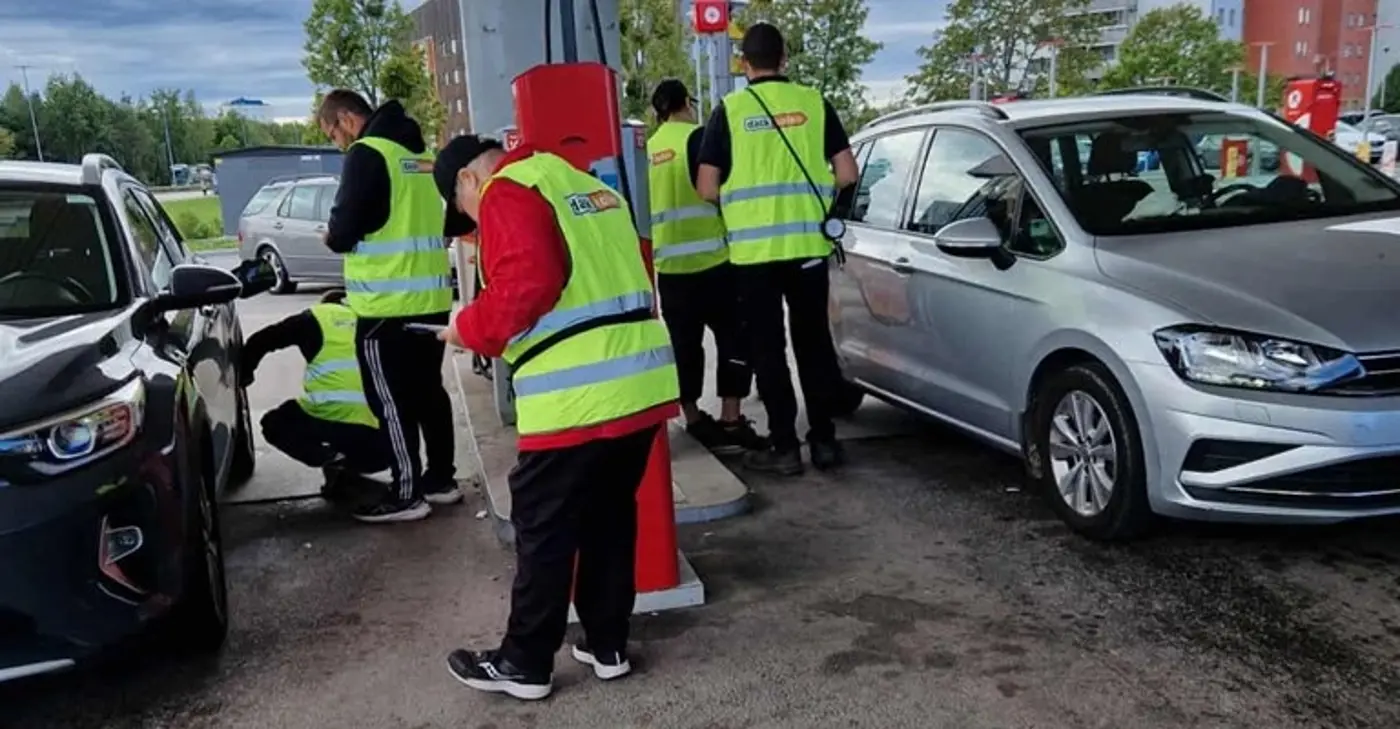Personer med reflexvästar pratar med bilförare på en bensinmack.