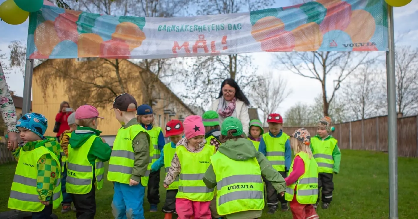En grupp förskolebarn med reflexvästar går baklänges in genom en målportal.