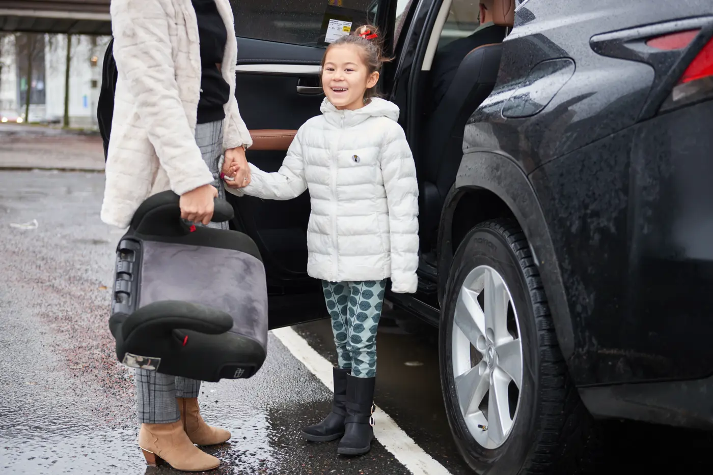 En mamma och ett barn är på väg att sätta sig i en taxi. I handen håller mamman en bälteskudde.