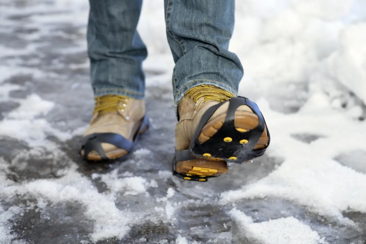 Närbild på ett par skor med halkskydd på slaskigt underlag.