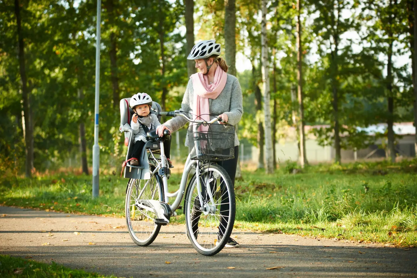 En mamma leder en cykel med sitt barn sittandes på en cykelsits.