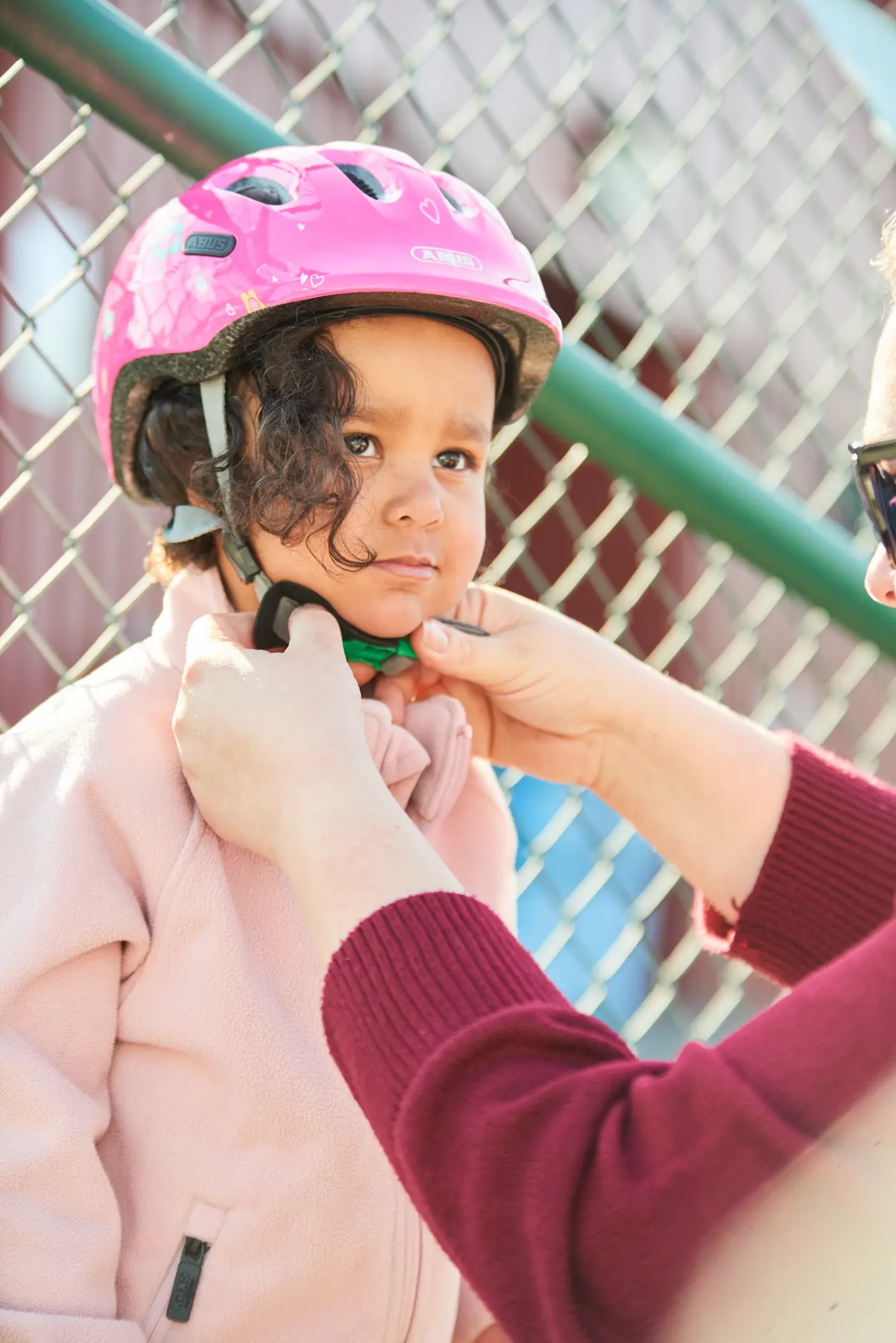 Ett småbarn får hjälp att knäppa sin cykelhjälm med grönt spänne