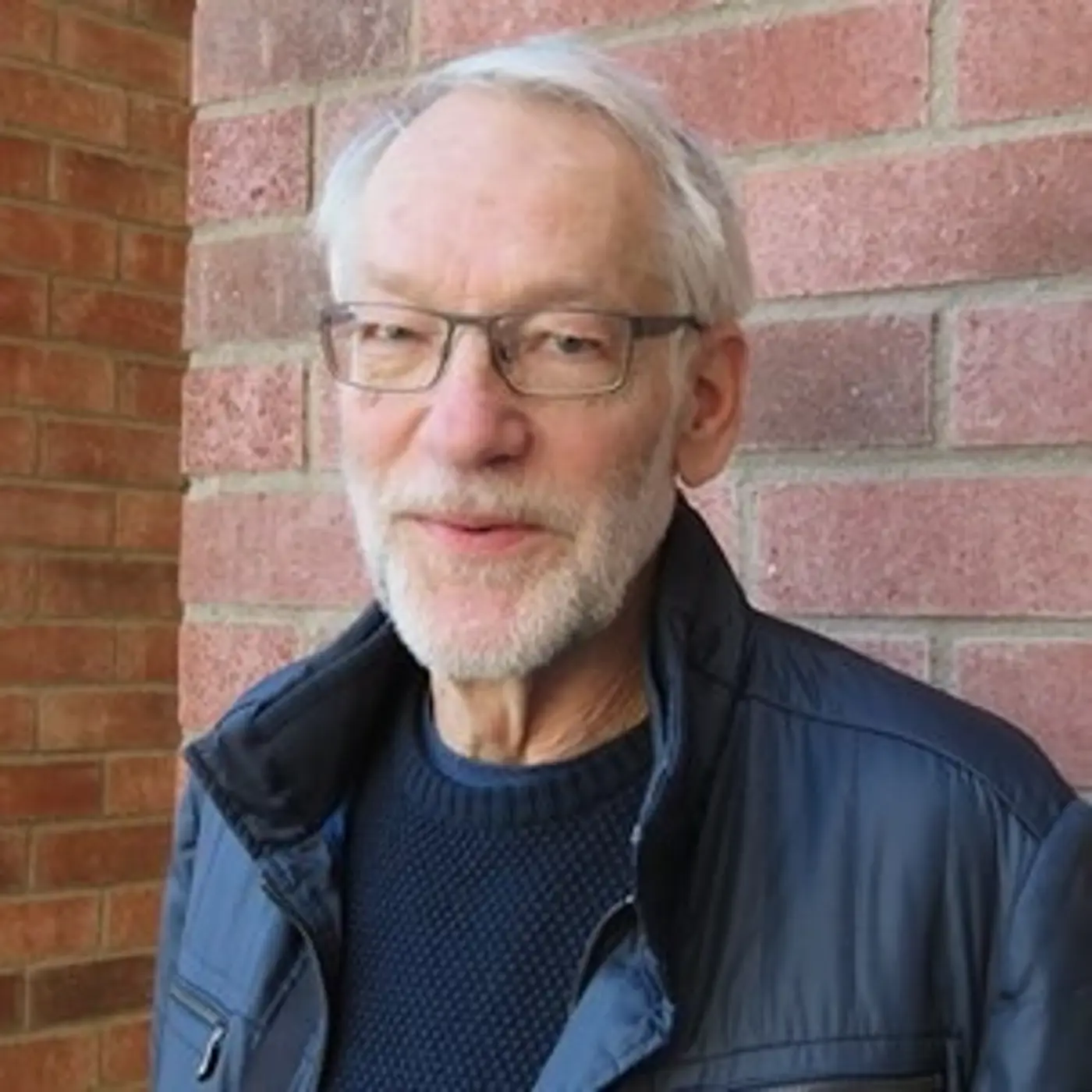 En leende äldre man med kort vitt skägg och glasögon.