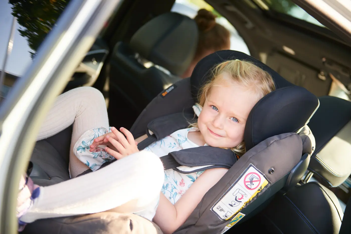 Ett barn i femårsåldern sitter i en bakåtvänd bilbarnstol och ler mot kameran.