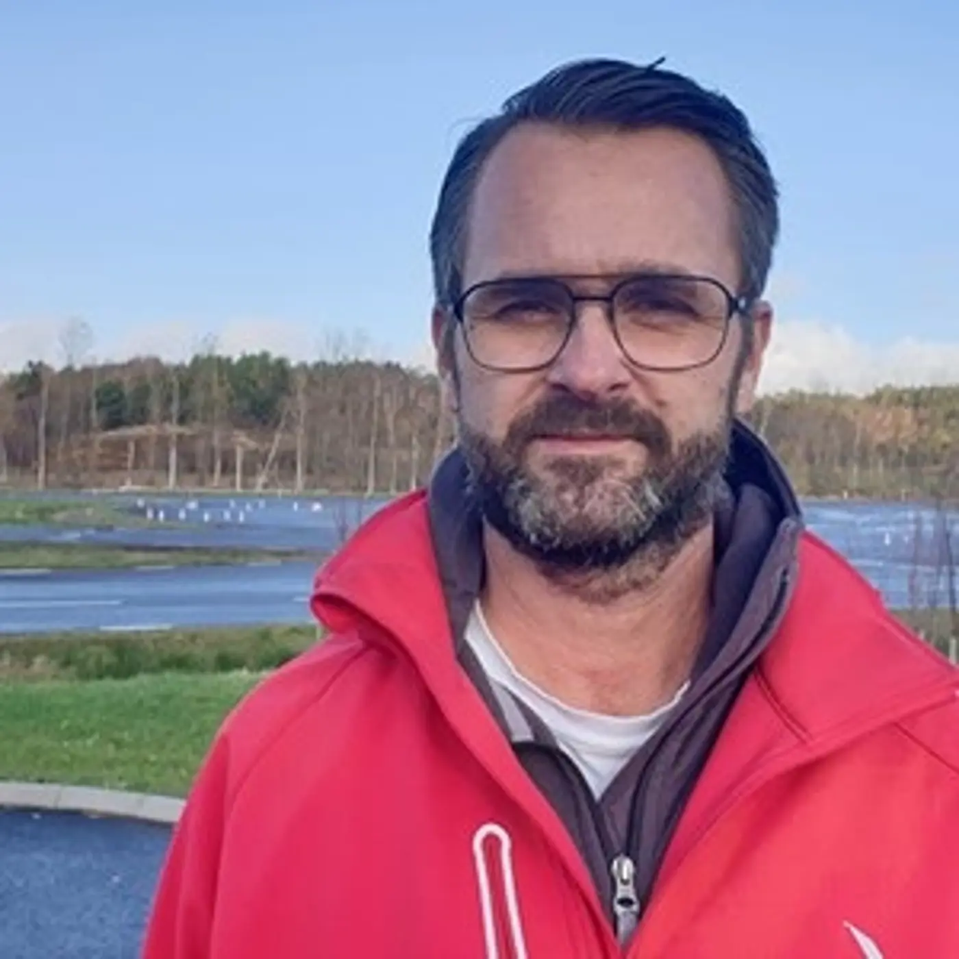 En man med glasögon och röd jacka.