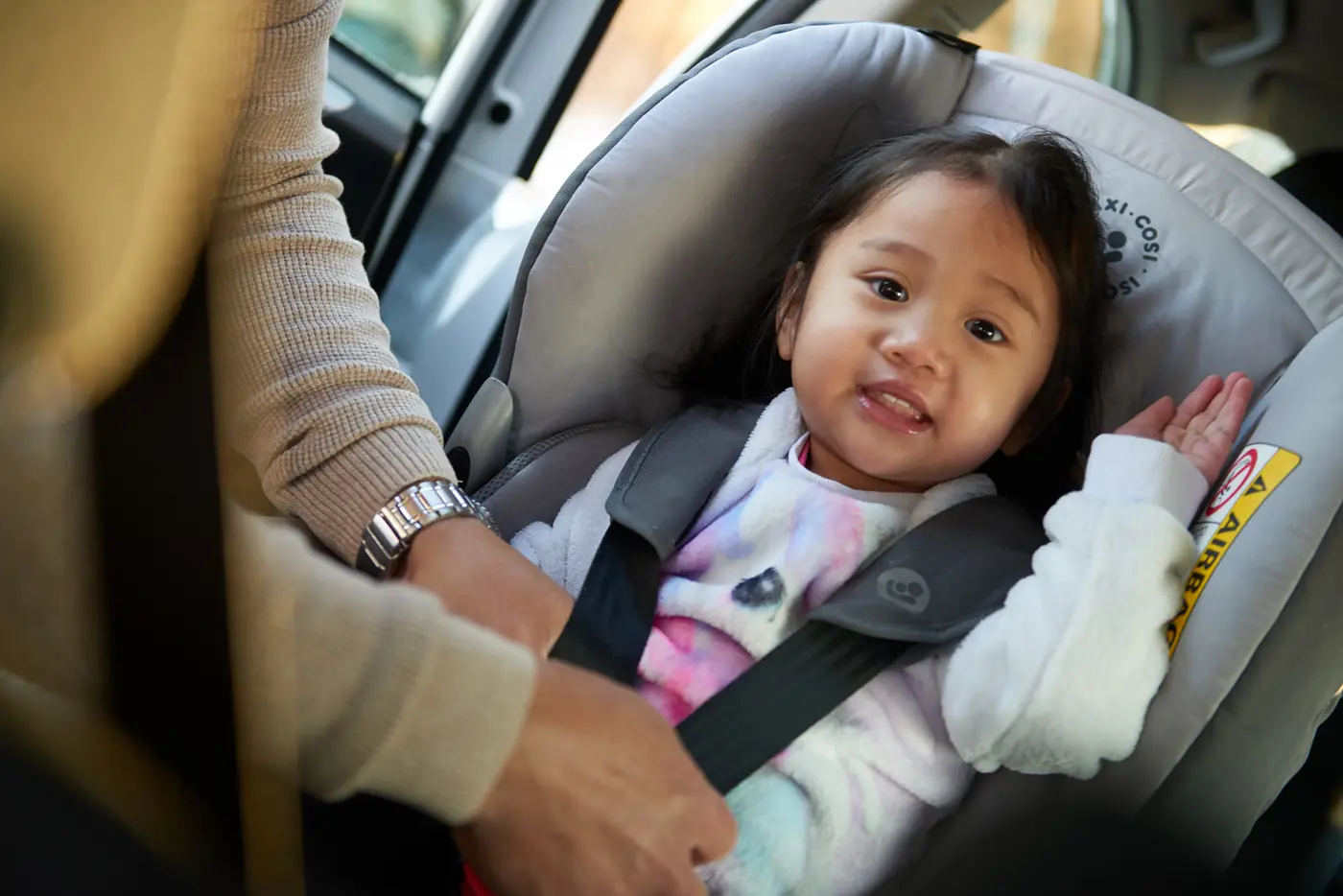 Ett småbarn sitter i en bakåtvänd bilbarnstol och får hjälp av en förälder att spänna säkerhetsbältet.