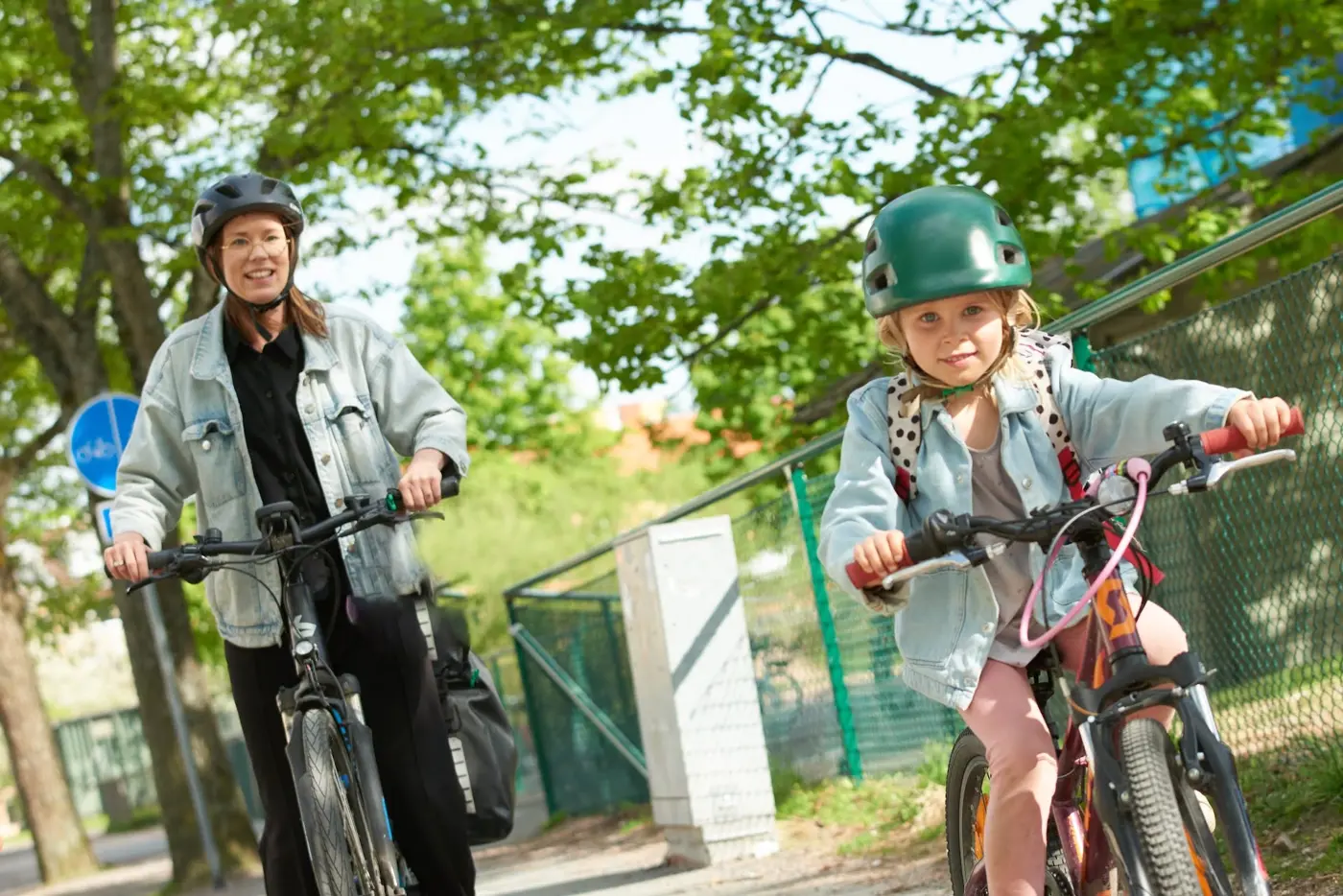 Ett barn och en förälder cyklar på en gång- och cykelbana. Båda har hjälm på huvudet.