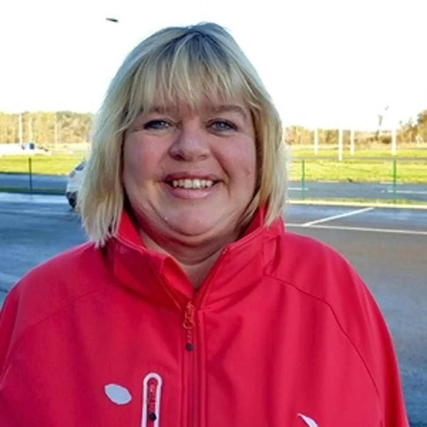 En leende kvinna med axelkort hår och röd jacka.