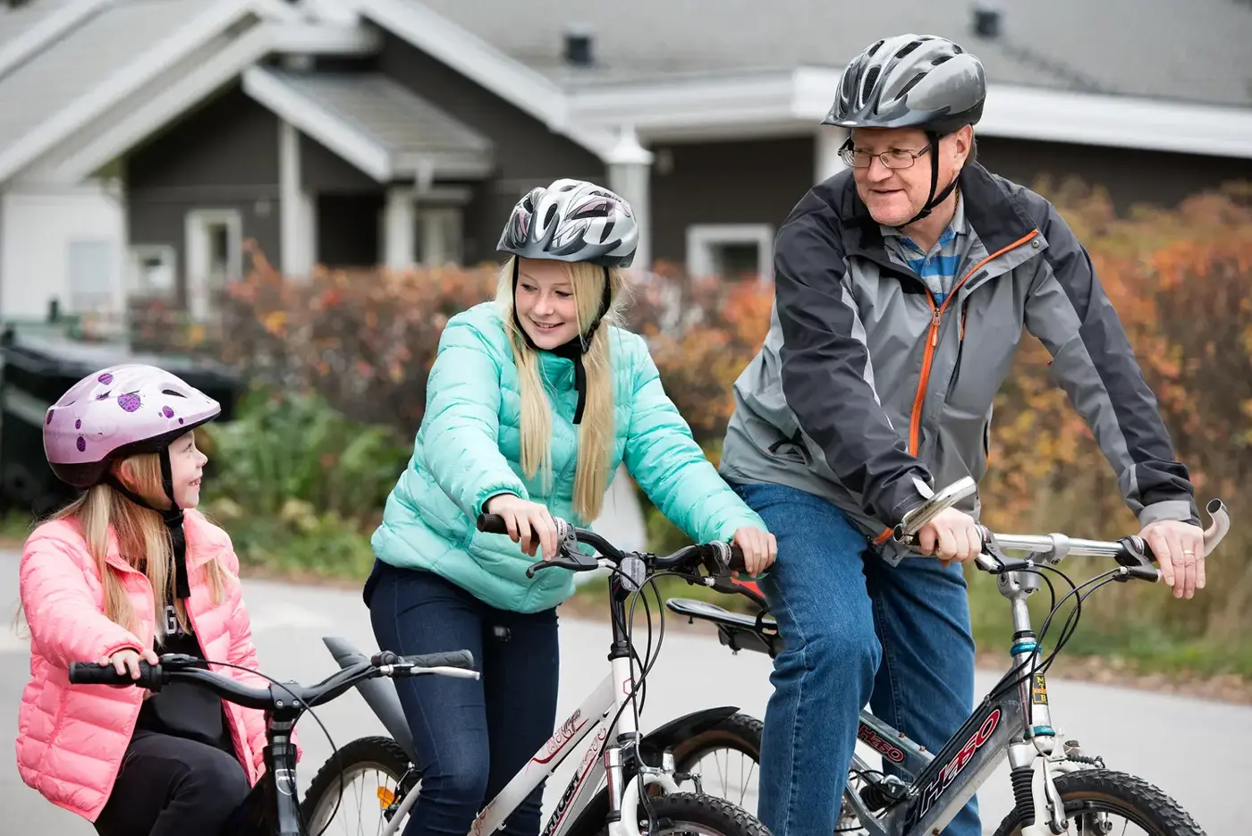 Ett barn, en tonåring och en vuxen sitter på varsin cykel i ett villaområde.