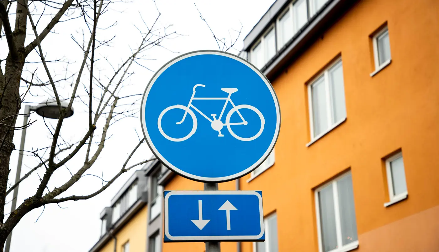 Blå vägskylt för påbjuden cykelbana. I bakgrunden ett orange lägenhetshus.