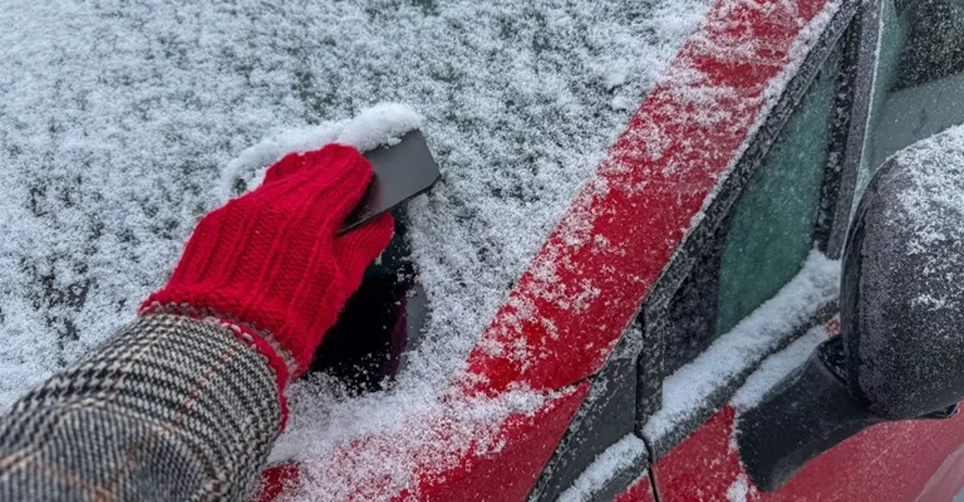 En person med vantar skrapar bort snö och is från en bilruta.