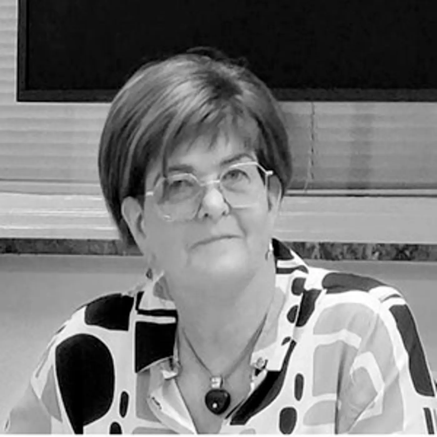 En kvinna med kort hår, glasögon och mönstrad blus.