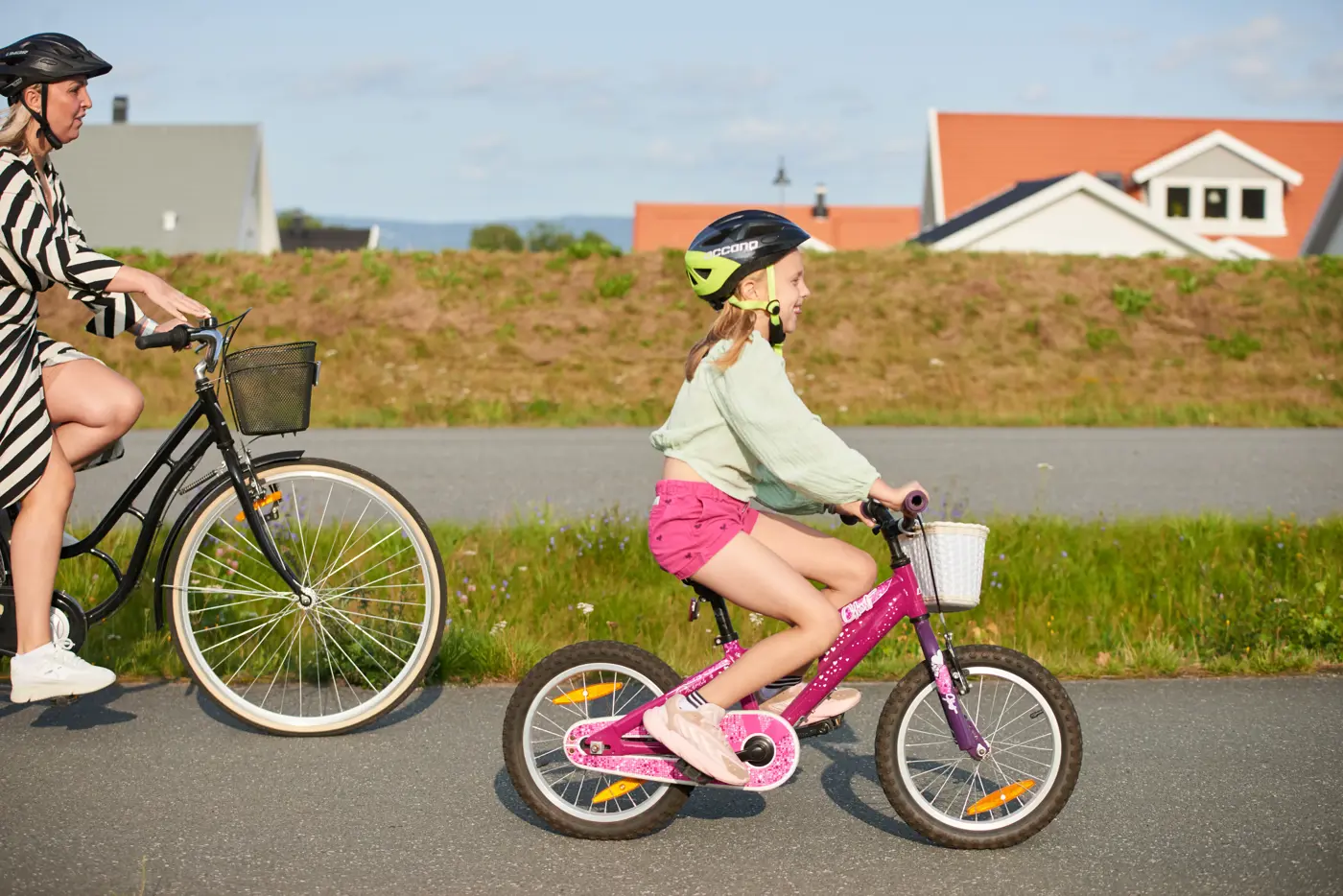 En vuxen och ett barn cyklar på en asfalterad cykelbana. Det är sommar och båda har hjälm på huvudet.