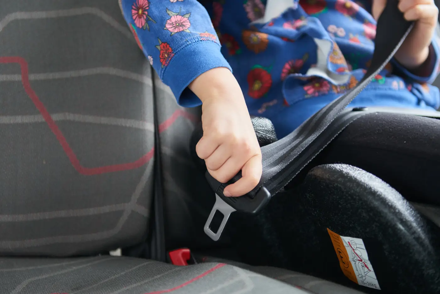 Ett barn sitter på en bälteskudde i en buss och spänner fast säkerhetsbältet.