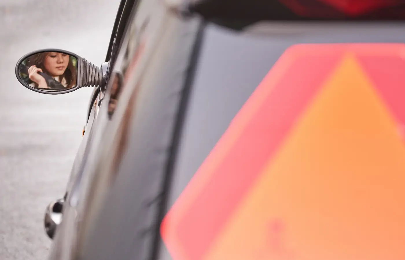 mopedbil bakifrån med LGF-skylt och ung kvinna syns i sidospegeln