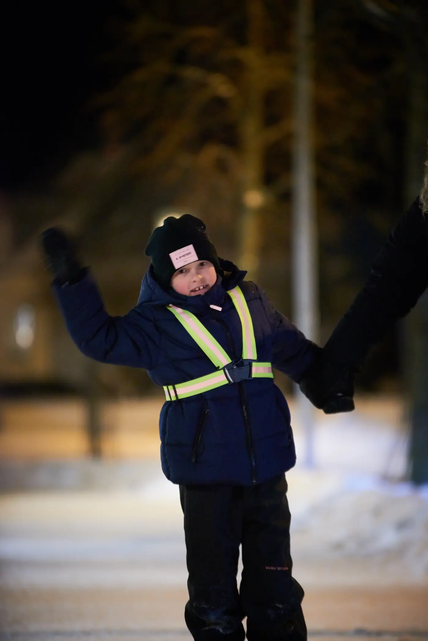 Ett barn med reflex och vinterkläder som vinkar. 
