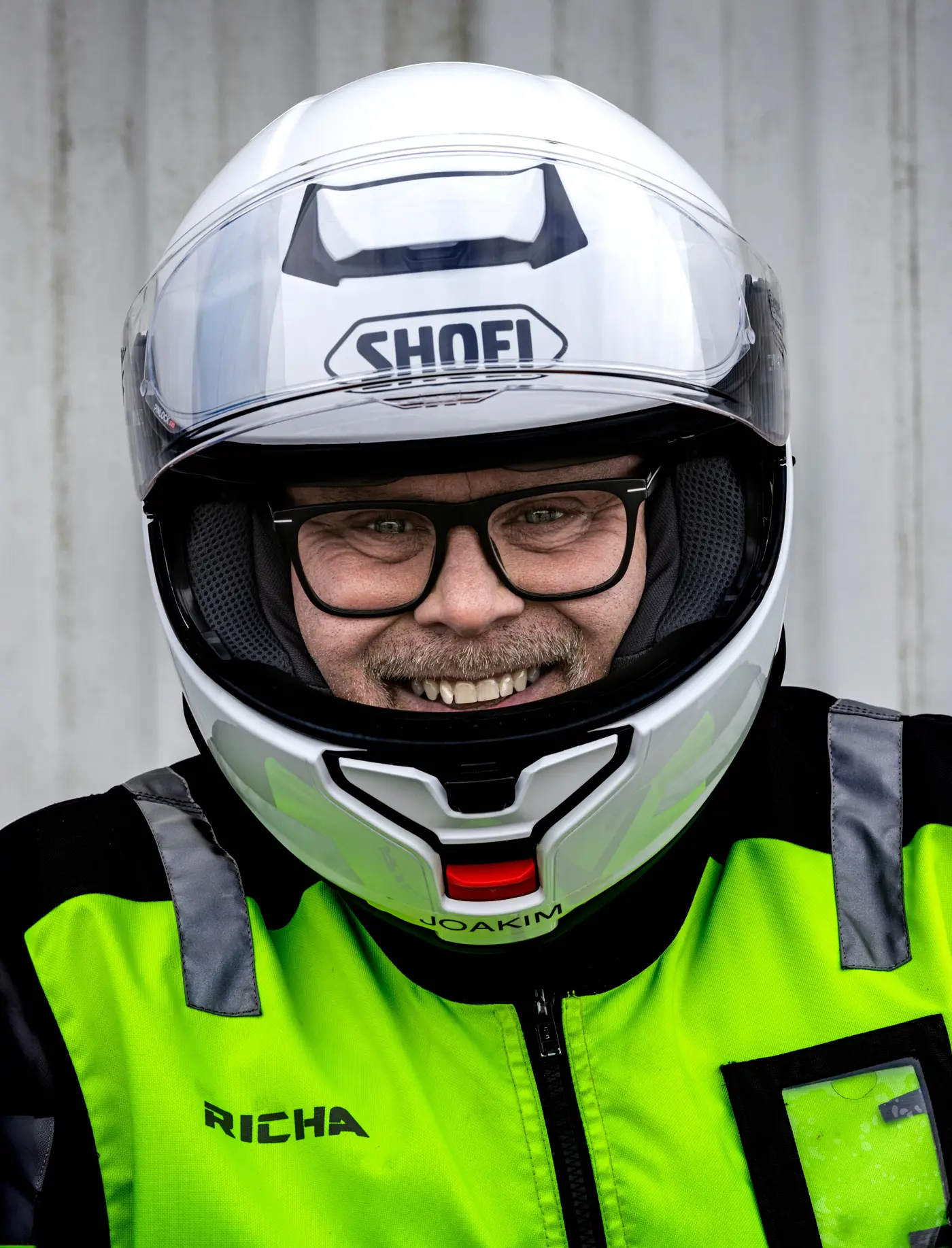 En porträttbild på en man med glasögon, varseljacka och motorcykelhjälm på huvudet.