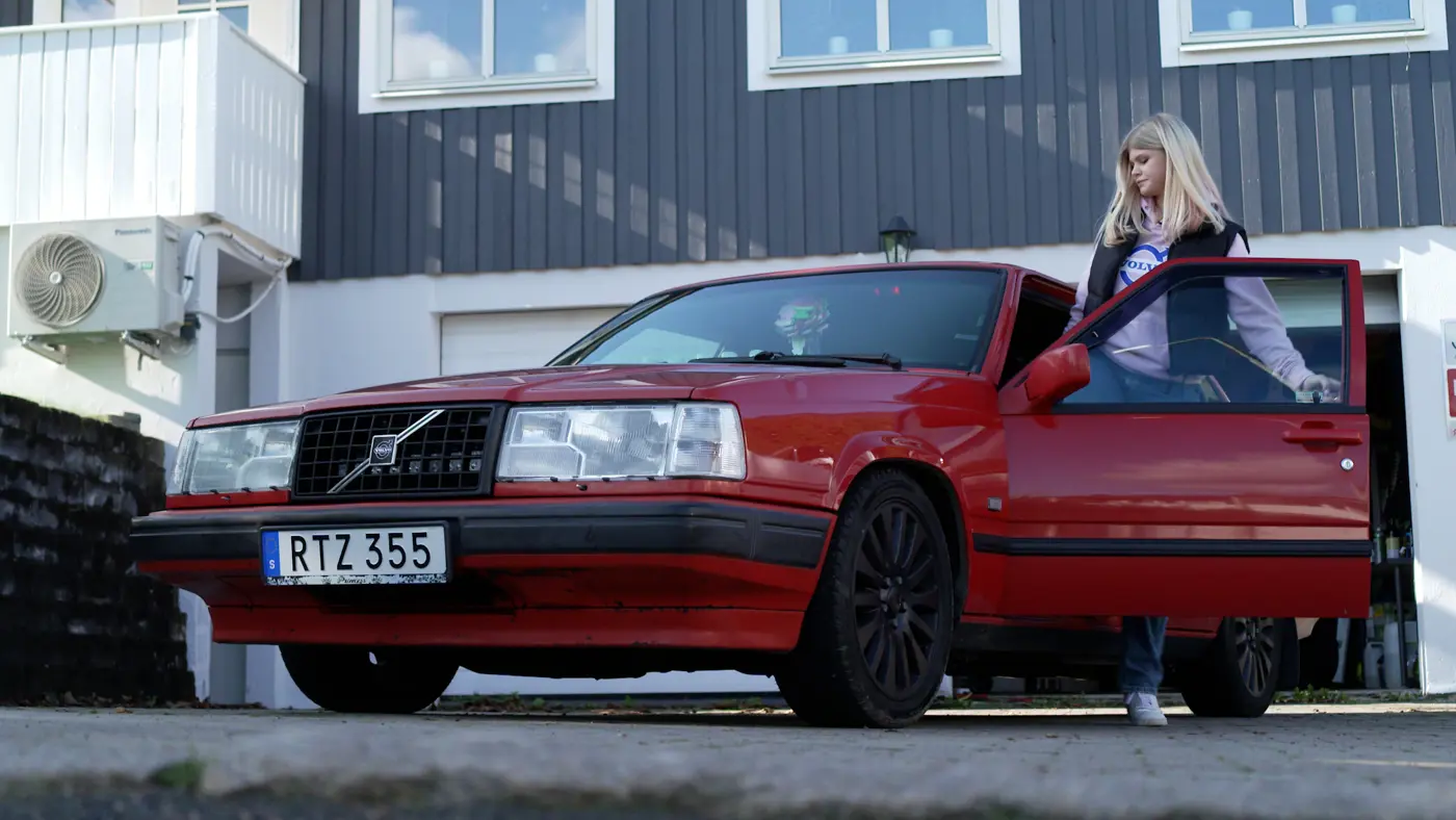 En ungdom är på väg att sätta sig i förarsätet i en röd A-traktor som står på uppfarten till ett hus.