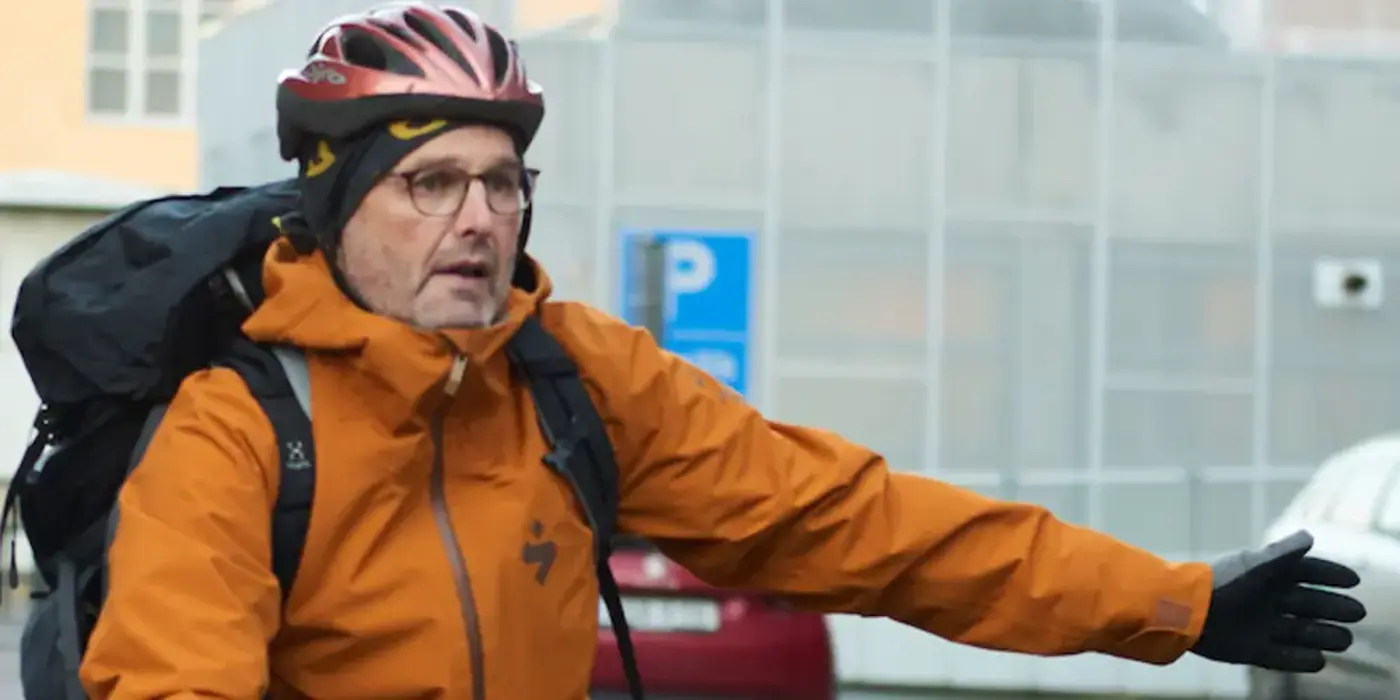 Person på cykel med hjälm på huvudet som signalerar med armen att den ska svänga vänster.