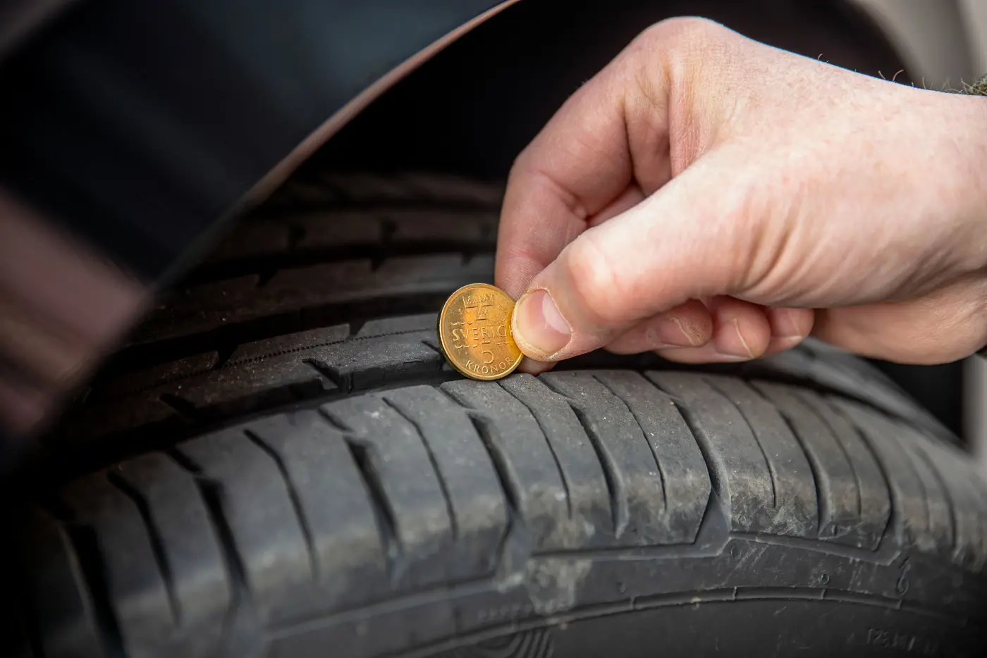 Kontroll av mönsterdjup på bildäck med en femkrona.