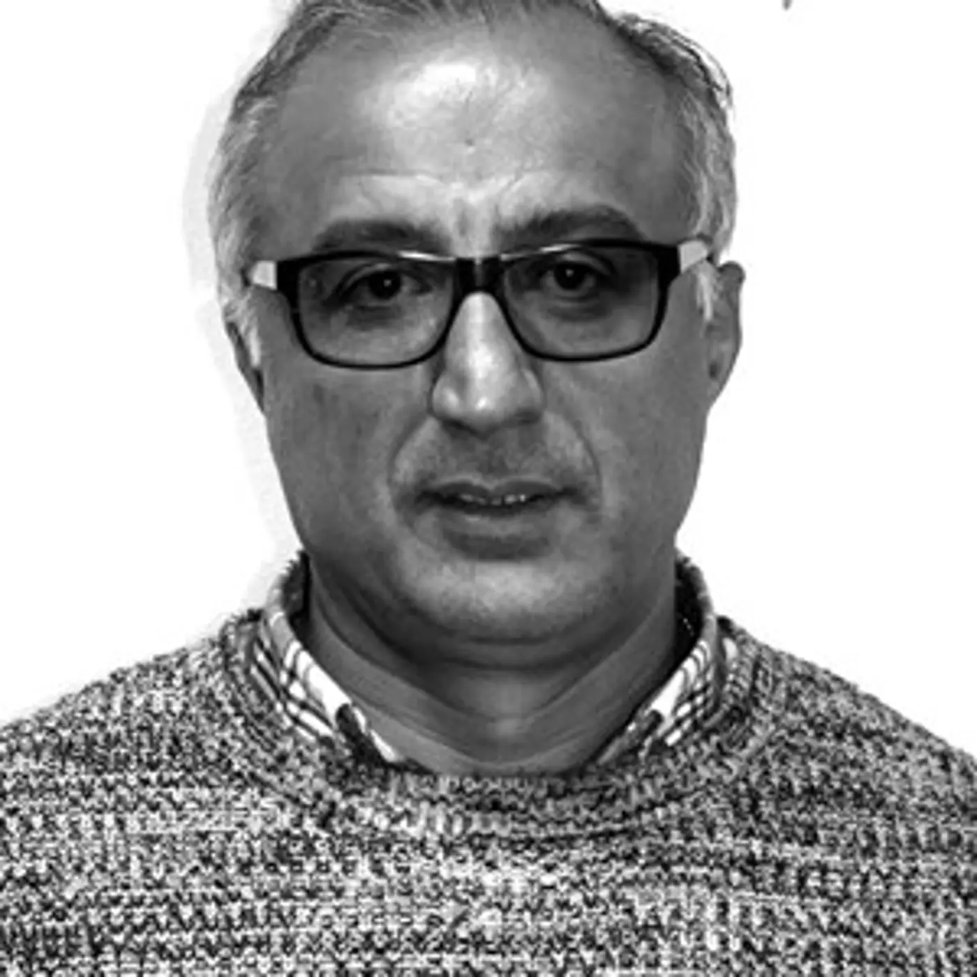 En äldre man med glasögon och stickad tröja.