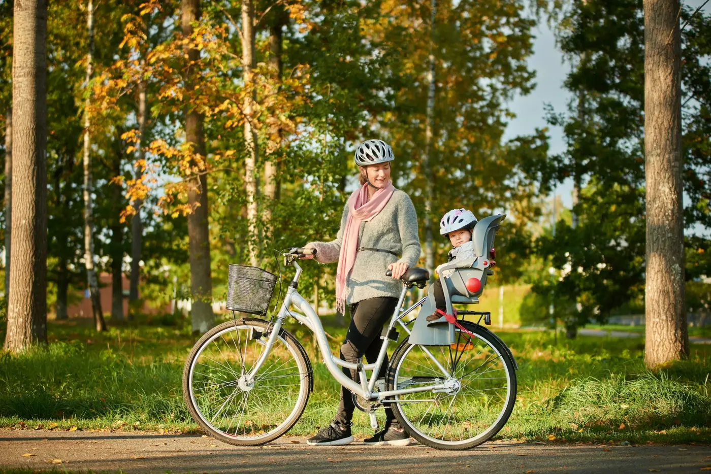 En mamma leder en cykel med sitt barn sittandes på en cykelsits.