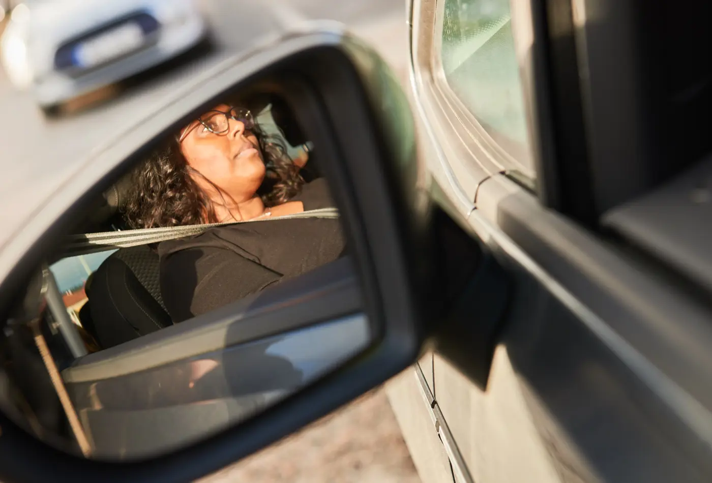 En backspegel på en bil reflekterar en kvinna som sitter i förarsätet på en bil med säkerhetsbältet fastspänt.