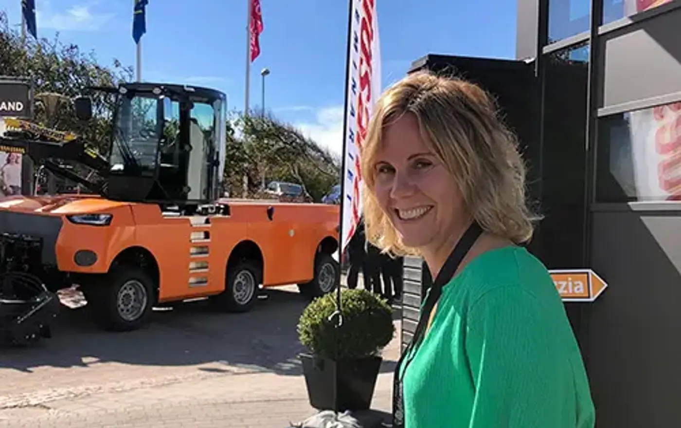 Leende person som står framför en grävmaskin